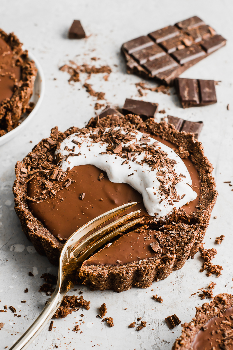 double chocolate vegan tarts with whipped cream and chocolate shavings on a grey background.