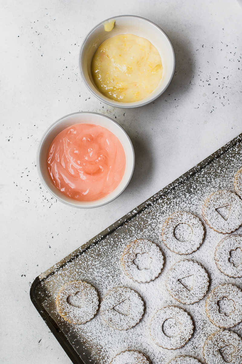 lemon and grapefruit curd in bowls on white background and Linzer cookies on baking sheet