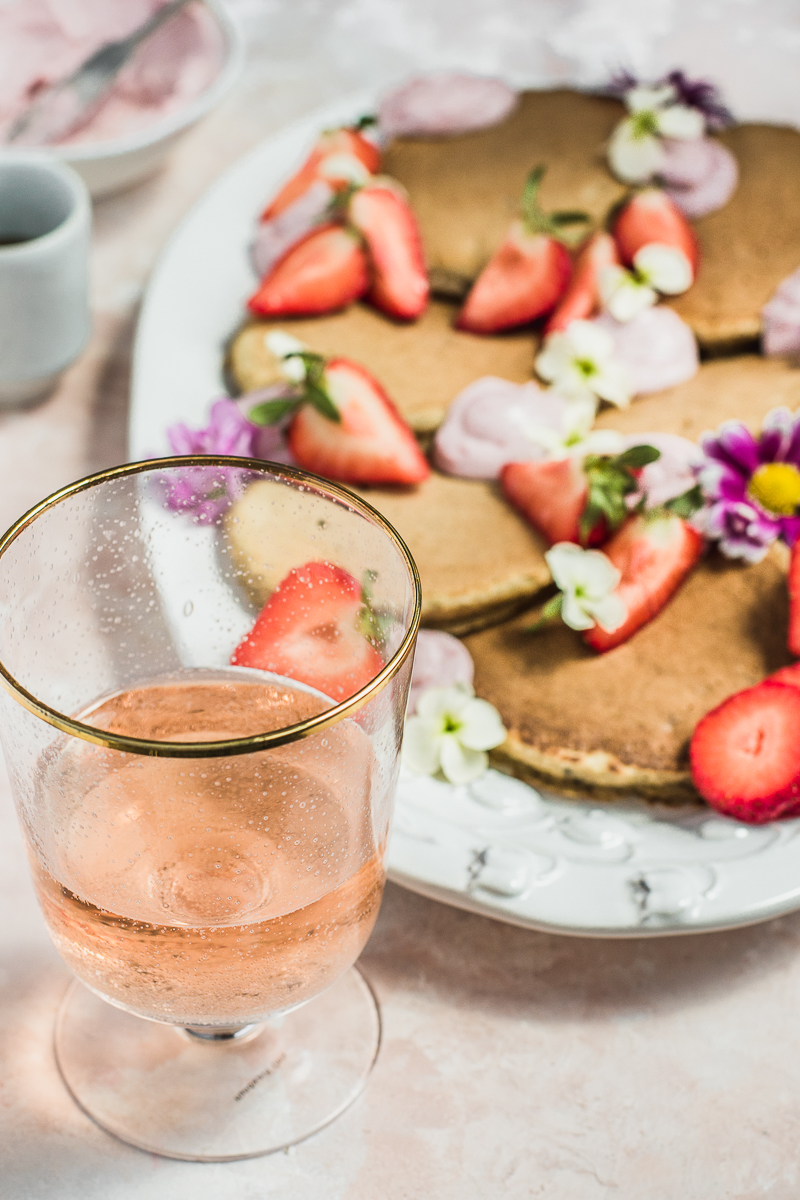 pancakes with strawberries on a white platter and a glass of wine