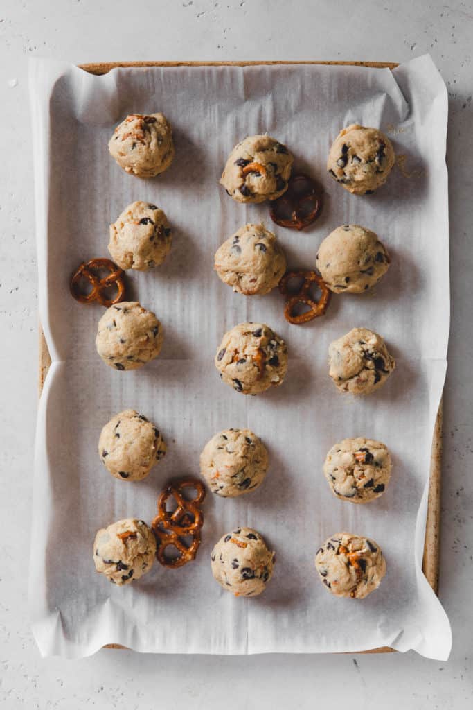cookie dough balls on a baking sheet lined with parchment paper and pretzels