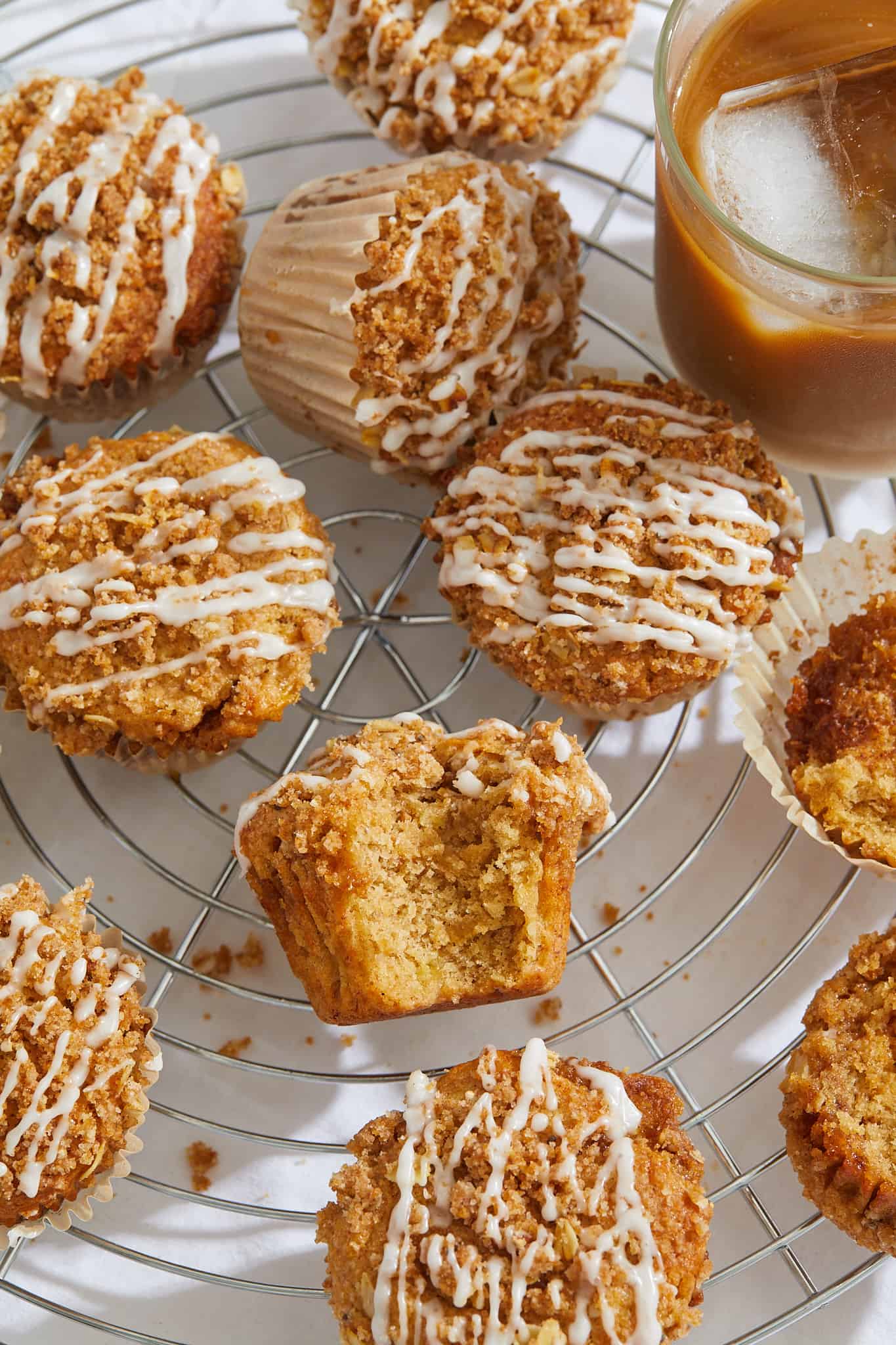 a cooling rack with cinnamon streusel muffins and sweet glaze with a big bite taken out of the center muffin