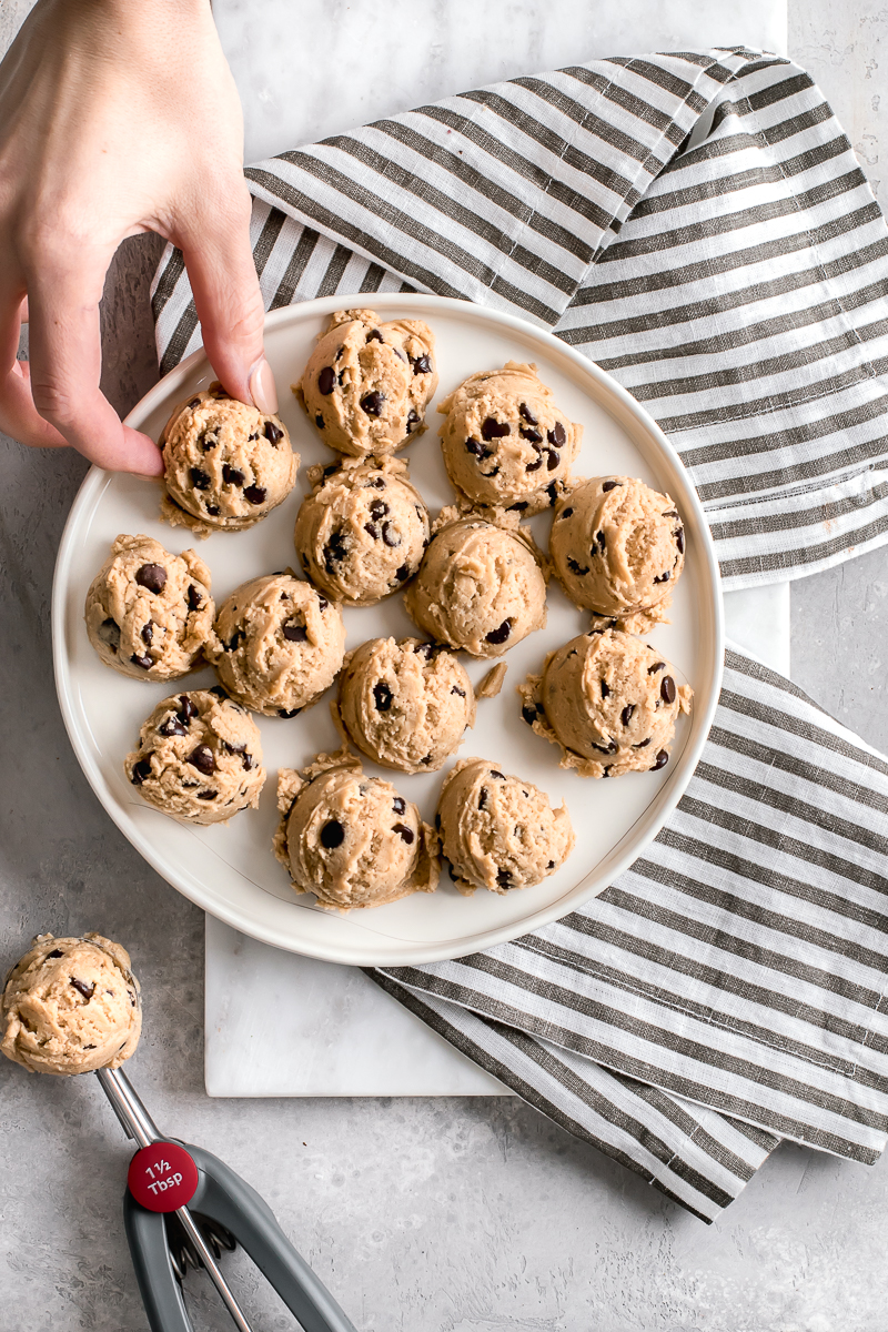 hand grabbing cookie dough from a white plate and cookie scooper