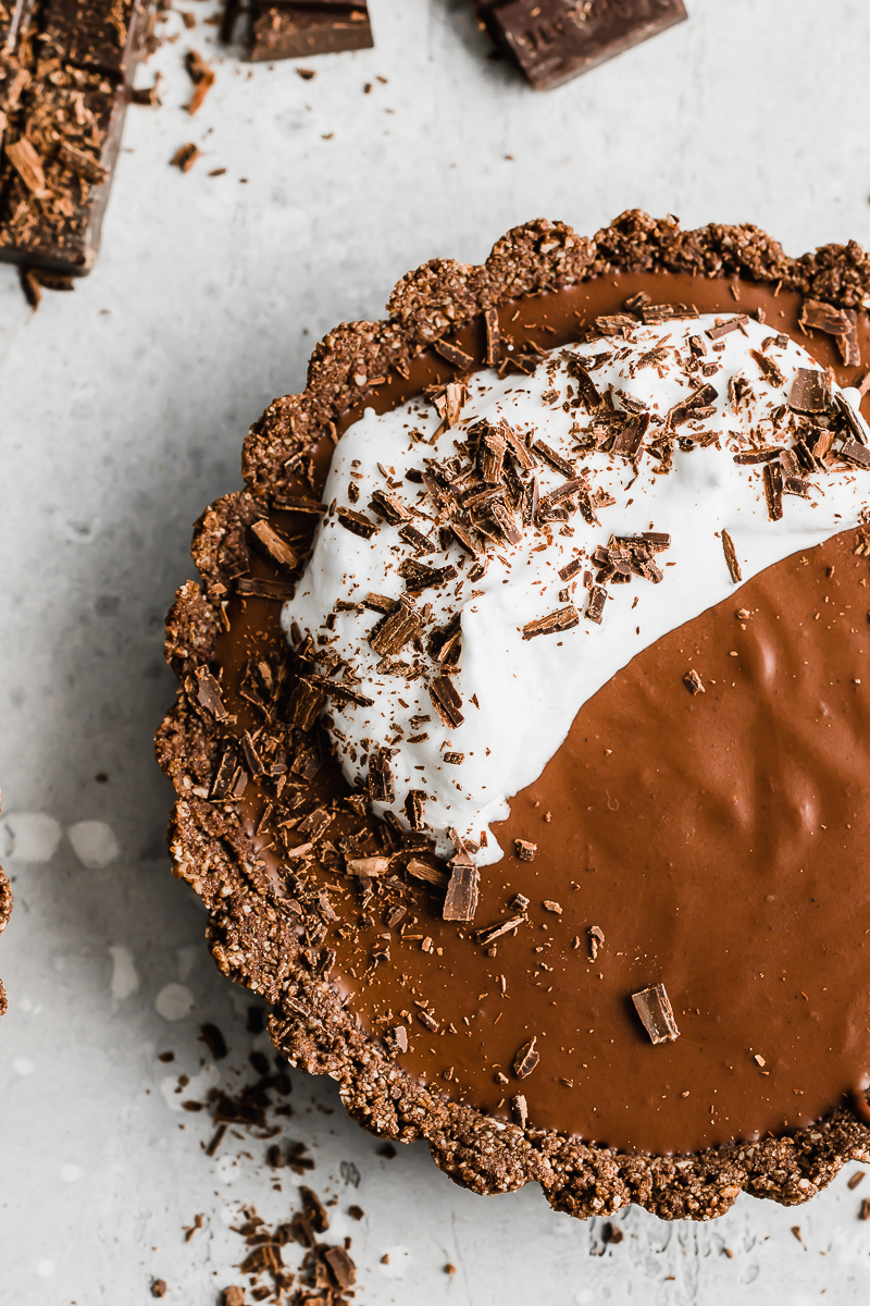 double chocolate vegan tarts with whipped cream and chocolate shavings on a grey background.