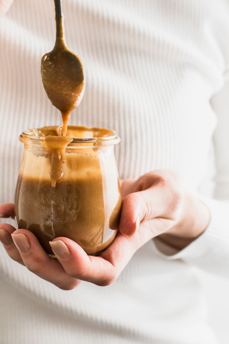 hand holding vegan caramel sauce in a jar and dripping from a spoon 