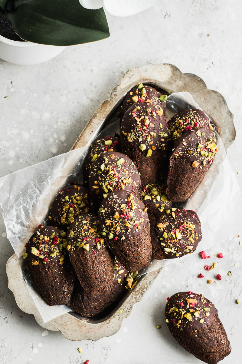 Chocolate madeleines with chocolate and crushed pistachios on a grey background.
