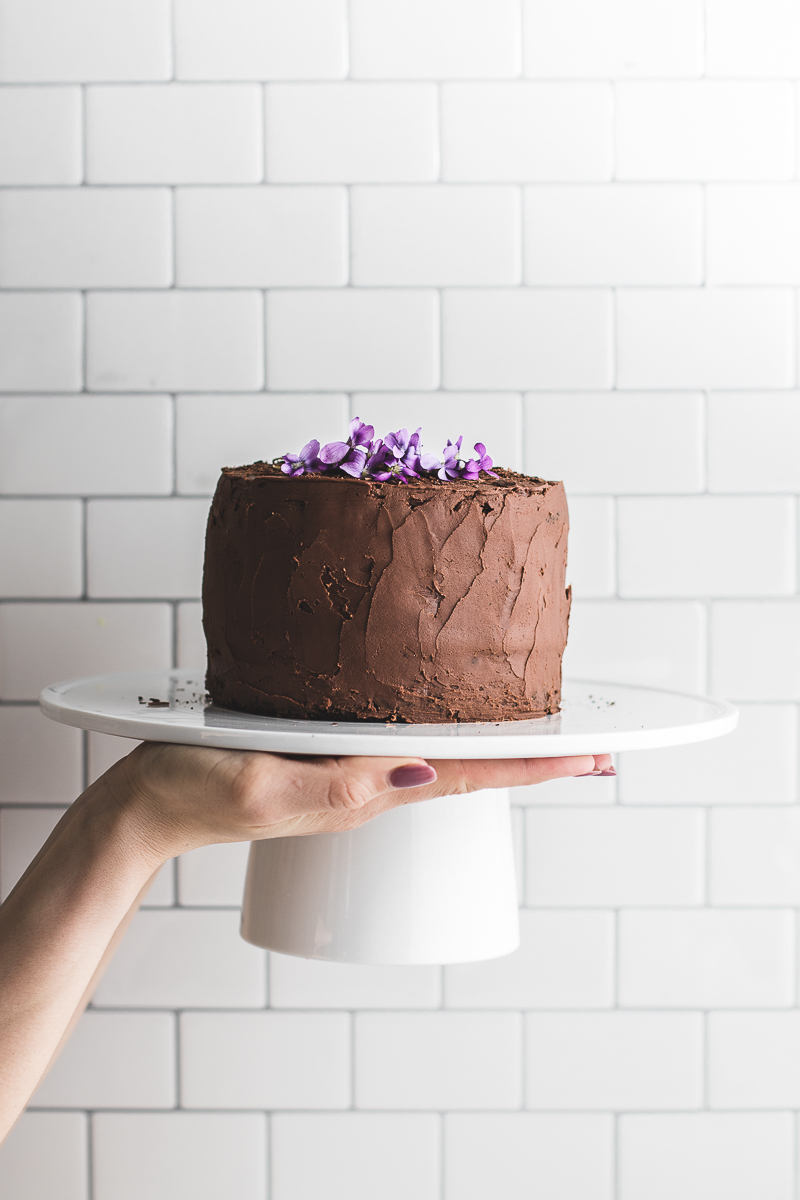 Hands holding up cake stand with chocolate cake and purple flours