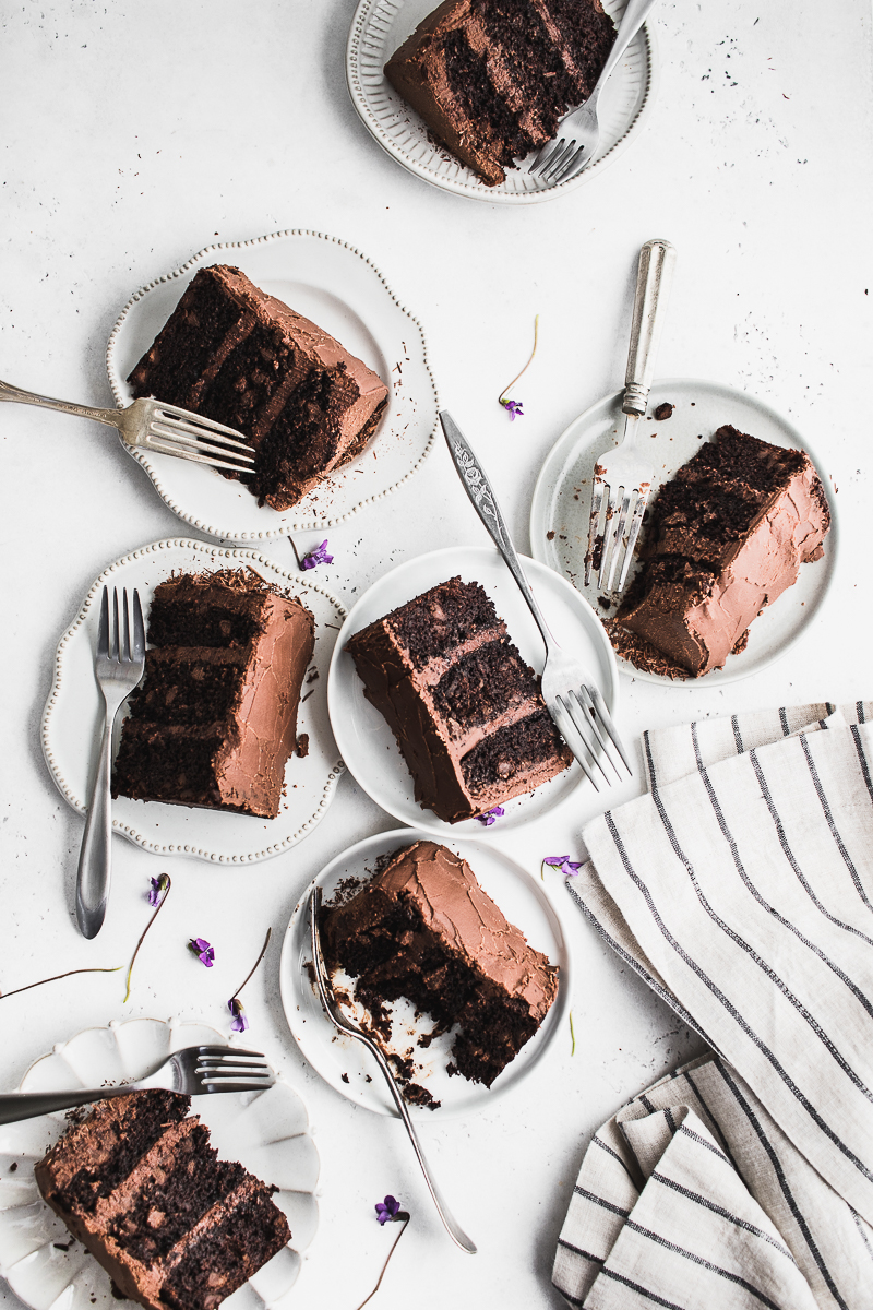 seven slices of chocolate cake on plates with forks on white background