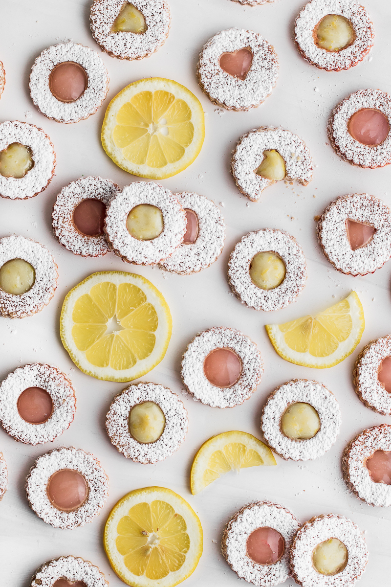 linzer cookies scattered on white backdrop with lemon slices