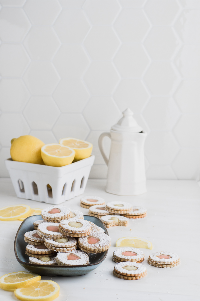 blue plate filled with linzer cookies and a bowl full of lemons