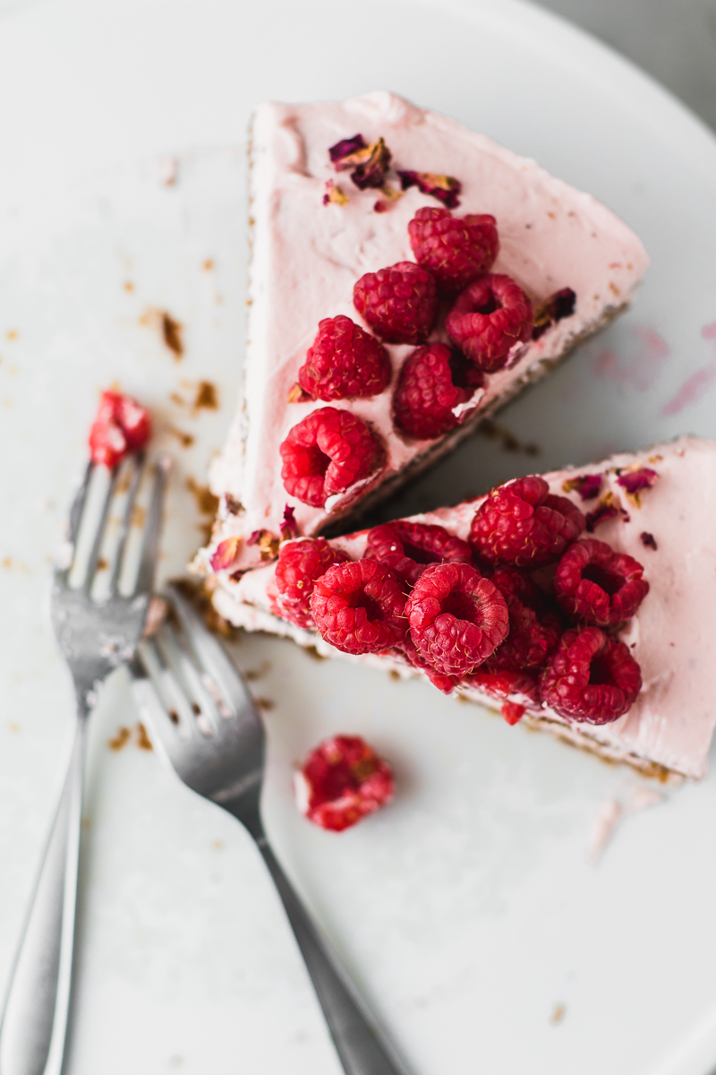 two slices of cake topped with raspberries and two forks.