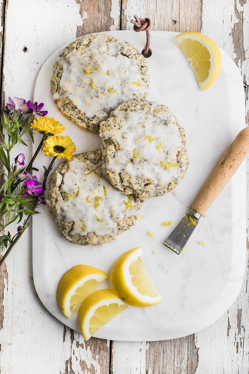 lemon scones with glaze on white wood and cutting board with flowers and lemons.