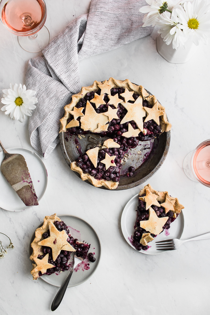 a slice of blueberry pie on a white surface with rosé
