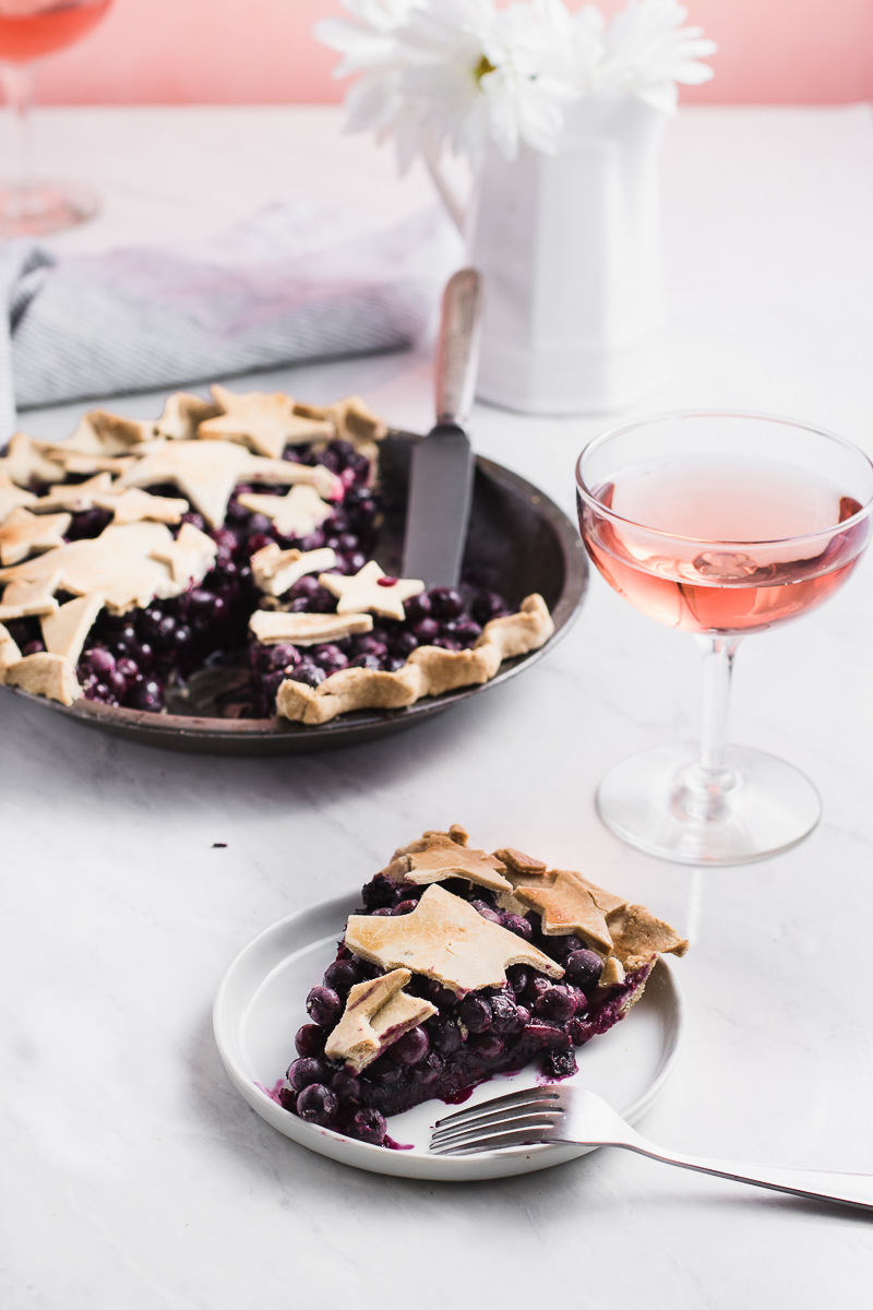 a slice of blueberry pie on a white surface with rosé