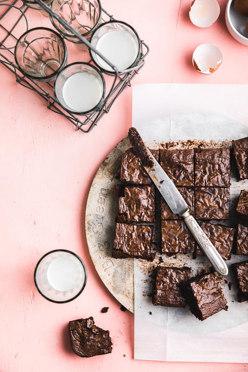 chocolate brownie squares on pink backdrop with cups of milk