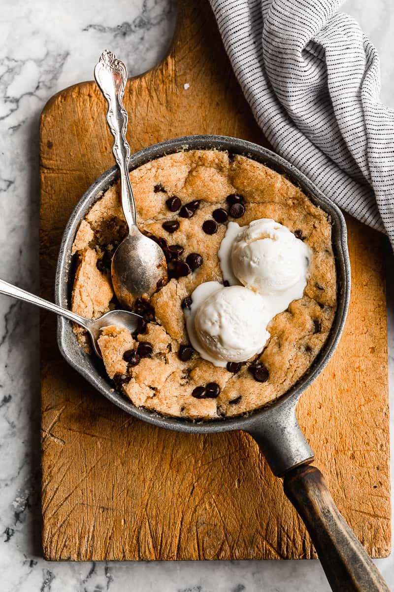 Skillet cookie gluten free with two spoons and scoops of ice cream on a cutting board.