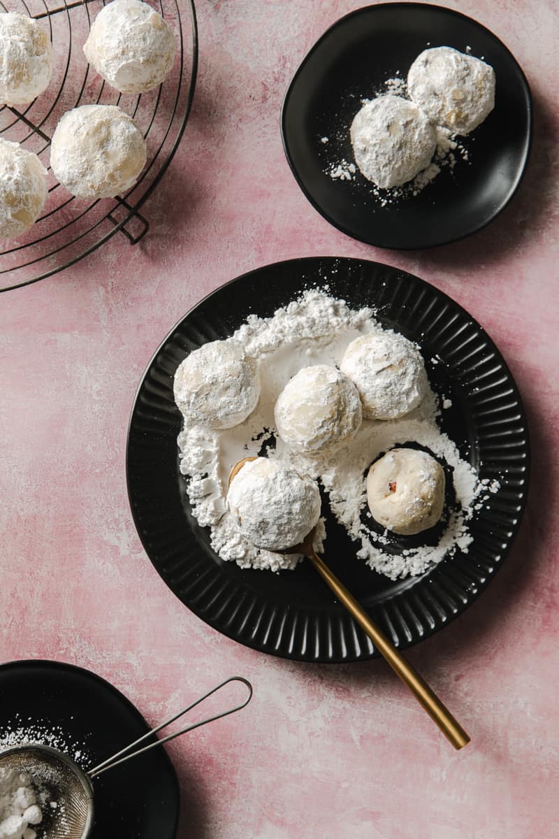 vegan snow ball cookies on a black plate. Buttery pecans and powdered sugar.