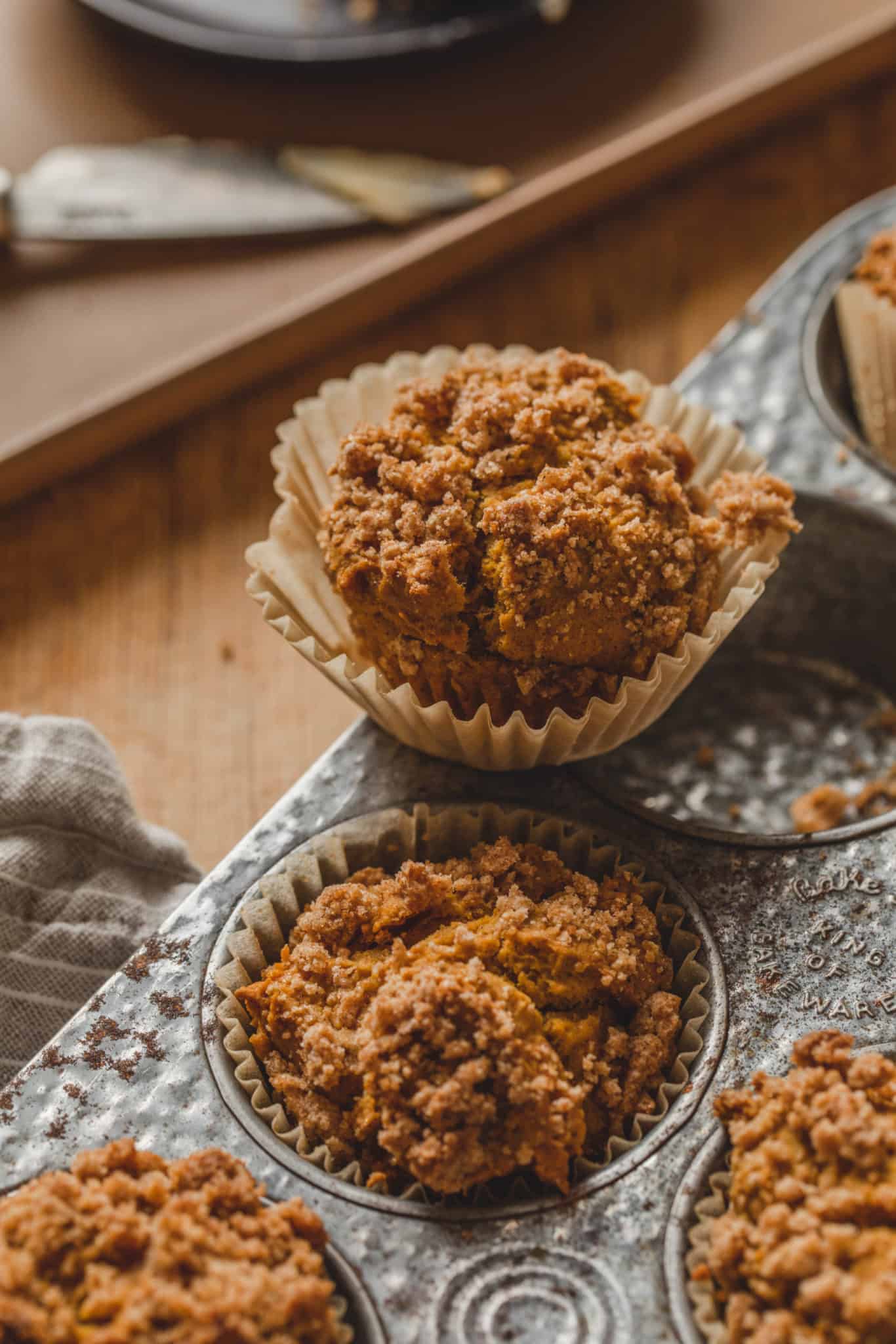 A vegan pumpkin muffin recipe with crumble topping sitting on a muffin pan.