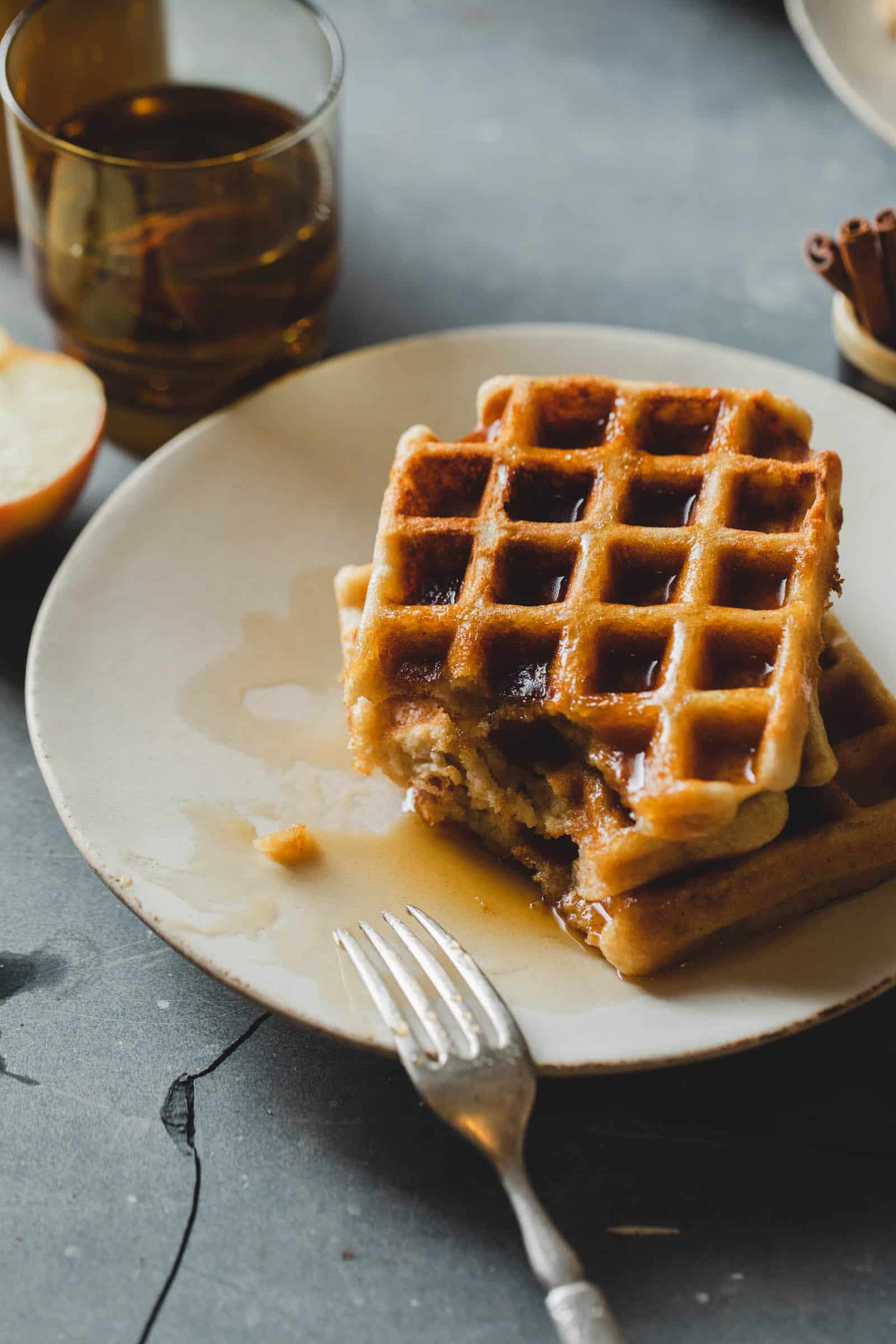 Platter of crispy vegan waffle recipe on plates with maple syrup and a giant bite taken out.