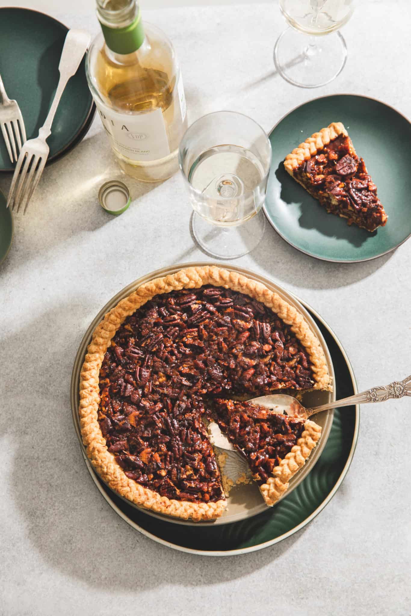 a dinner table with the best pecan pie recipe with slices on green plates and wine