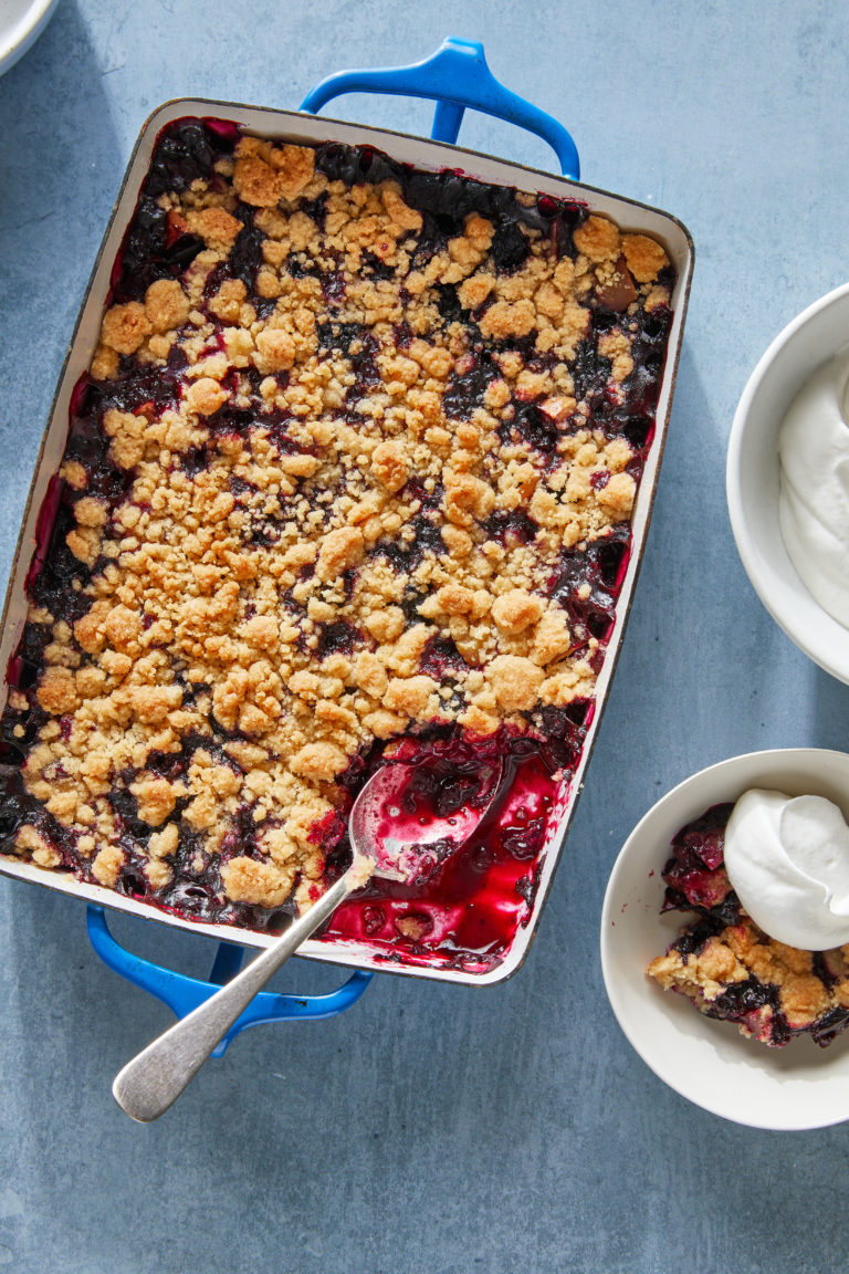 apple and blueberry crumble in a blue pan with spoons and cream