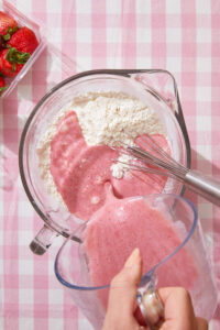 pink strawberry batter being poured into flour for a strawberry cake